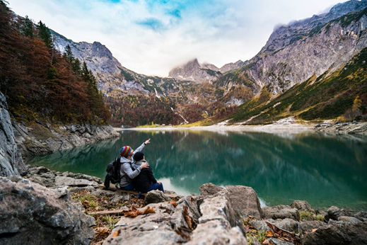Two hikers sitting on rocks beside a mountain lake